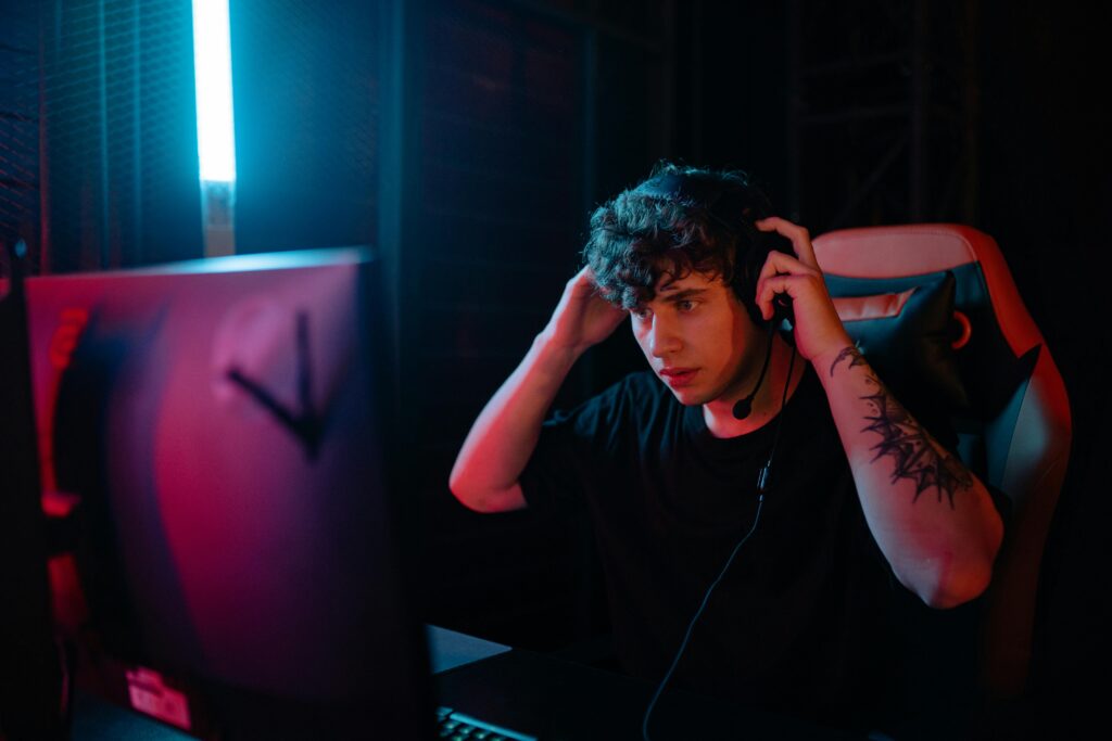 Tattooed man focused on gaming with headset at night.