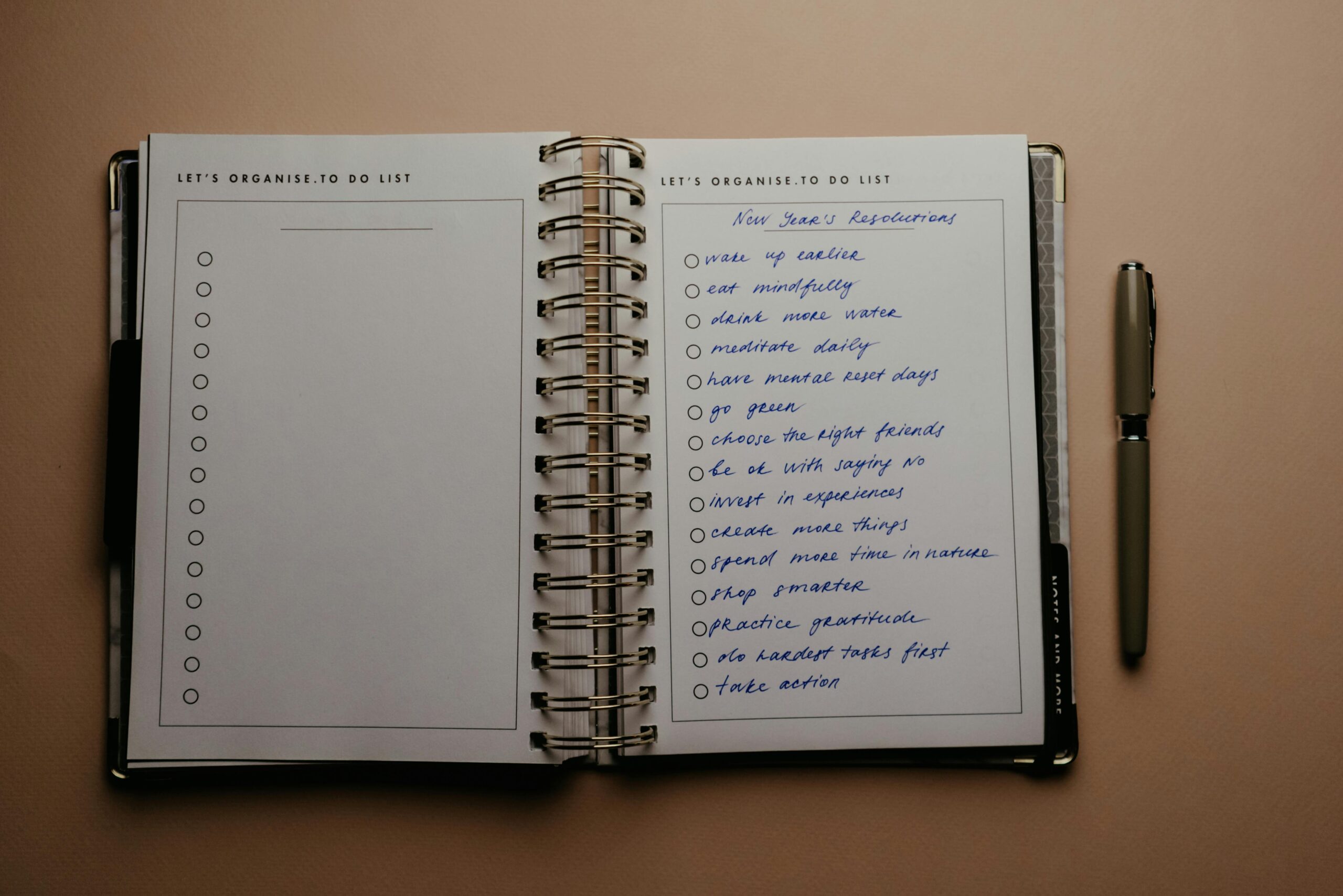 Open planner with New Year's resolutions, spiral binding, and pen on warm-toned background.