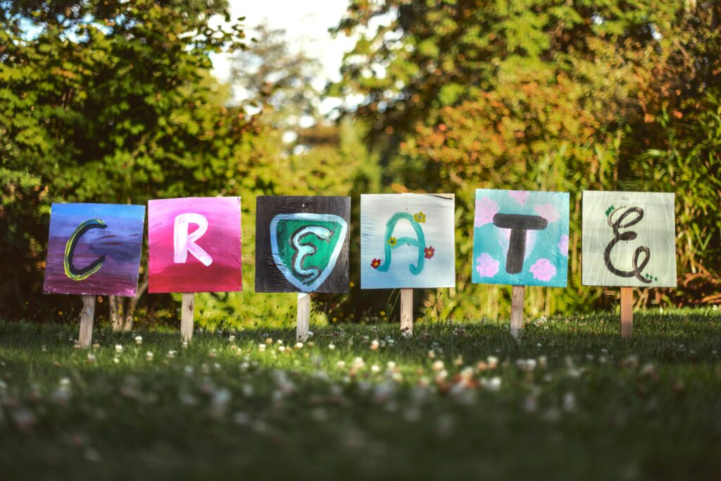 Vibrant painted signs spelling 'CREATE' in a lush outdoor garden setting.