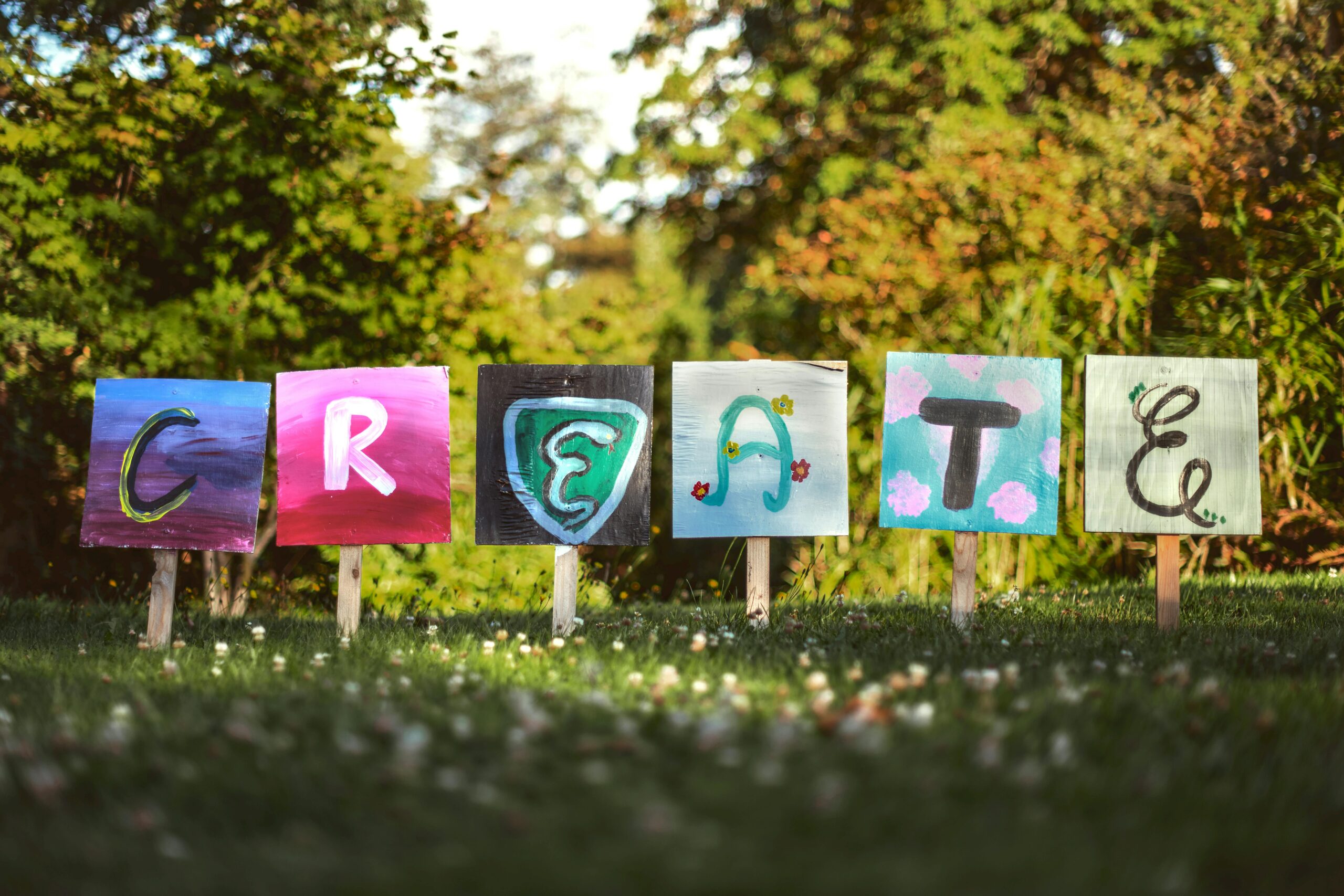 Vibrant painted signs spelling 'CREATE' in a lush outdoor garden setting.