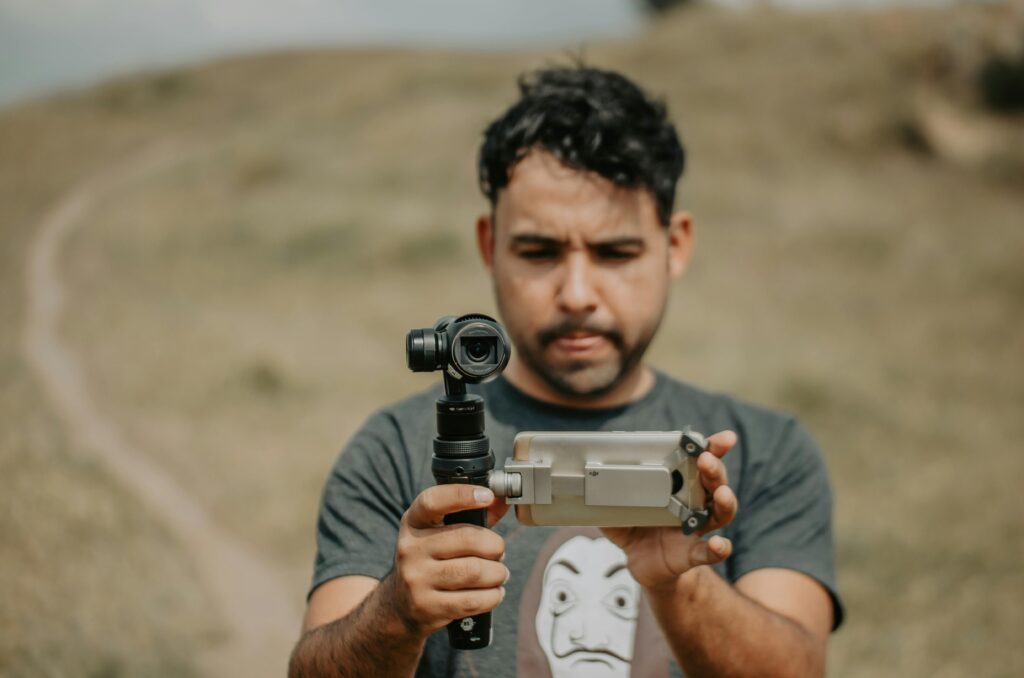 Man using a smartphone gimbal for videography on a grassy field.
